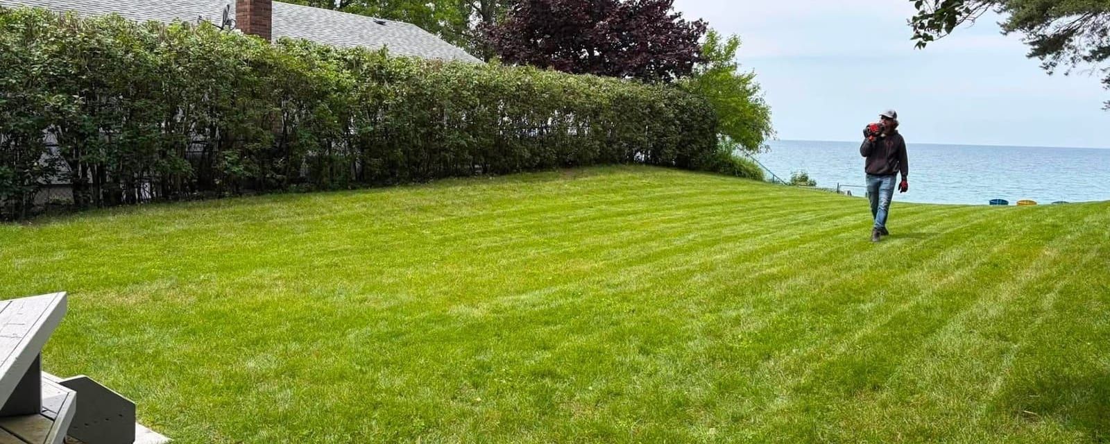 A crew member walking a large freshly striped lawn overlooking the water