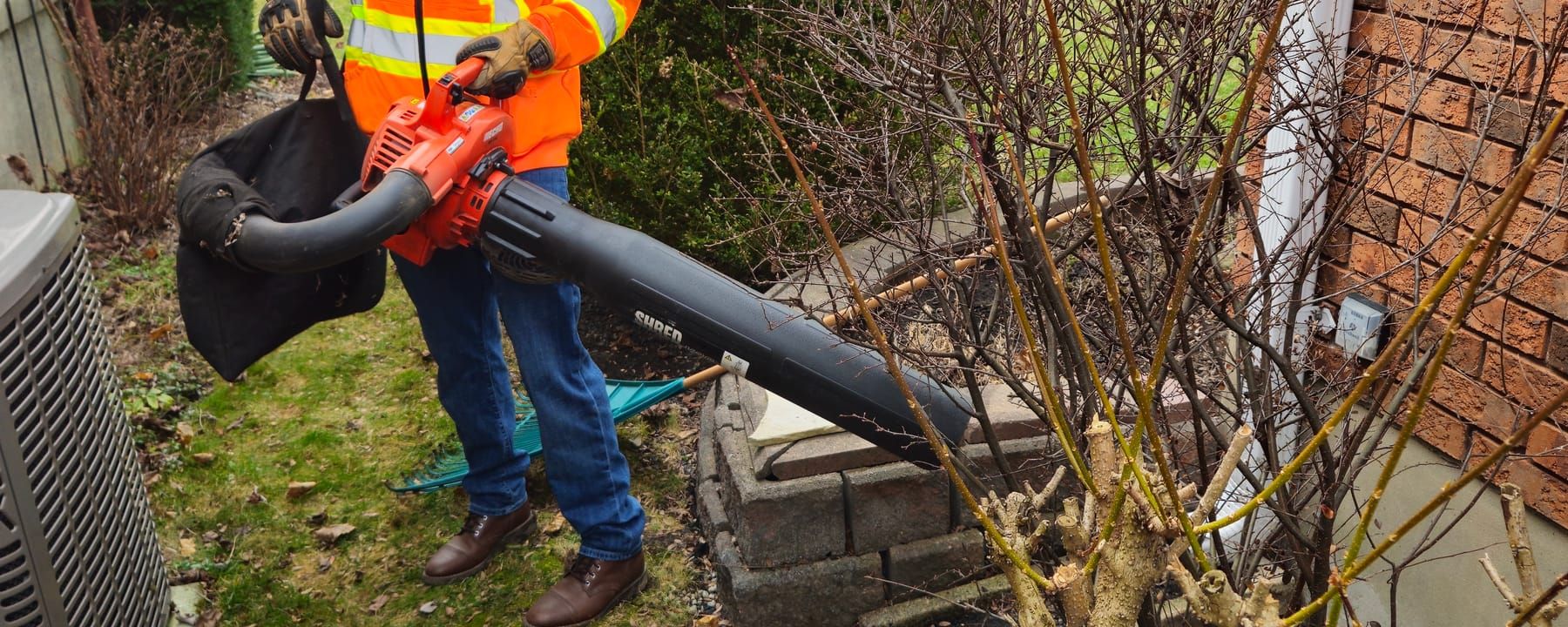 Crew member clearing leaves from a front garden bed with a backpack blower