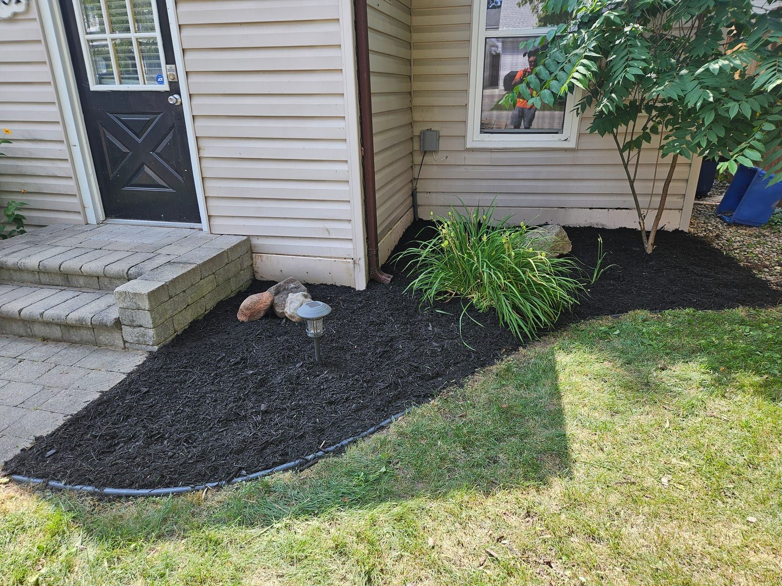 The same corner garden bed beside the side steps after cleanup, edged and topped with fresh black mulch