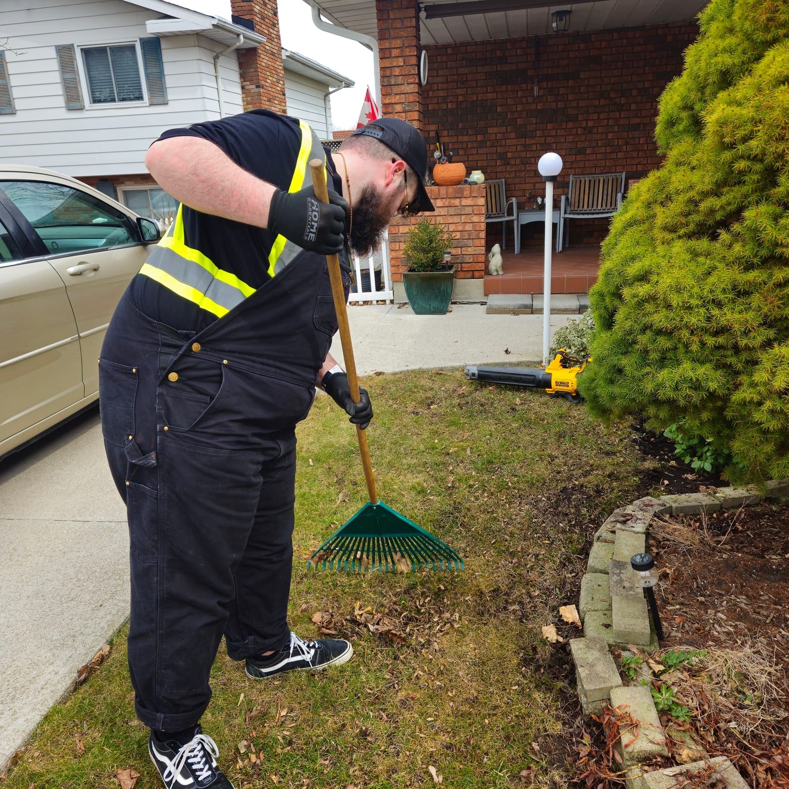 A crew member in high-visibility gear raking a front garden bed