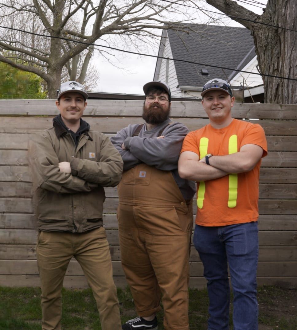 The Lambton Maintenance Men crew standing together in front of a wood fence