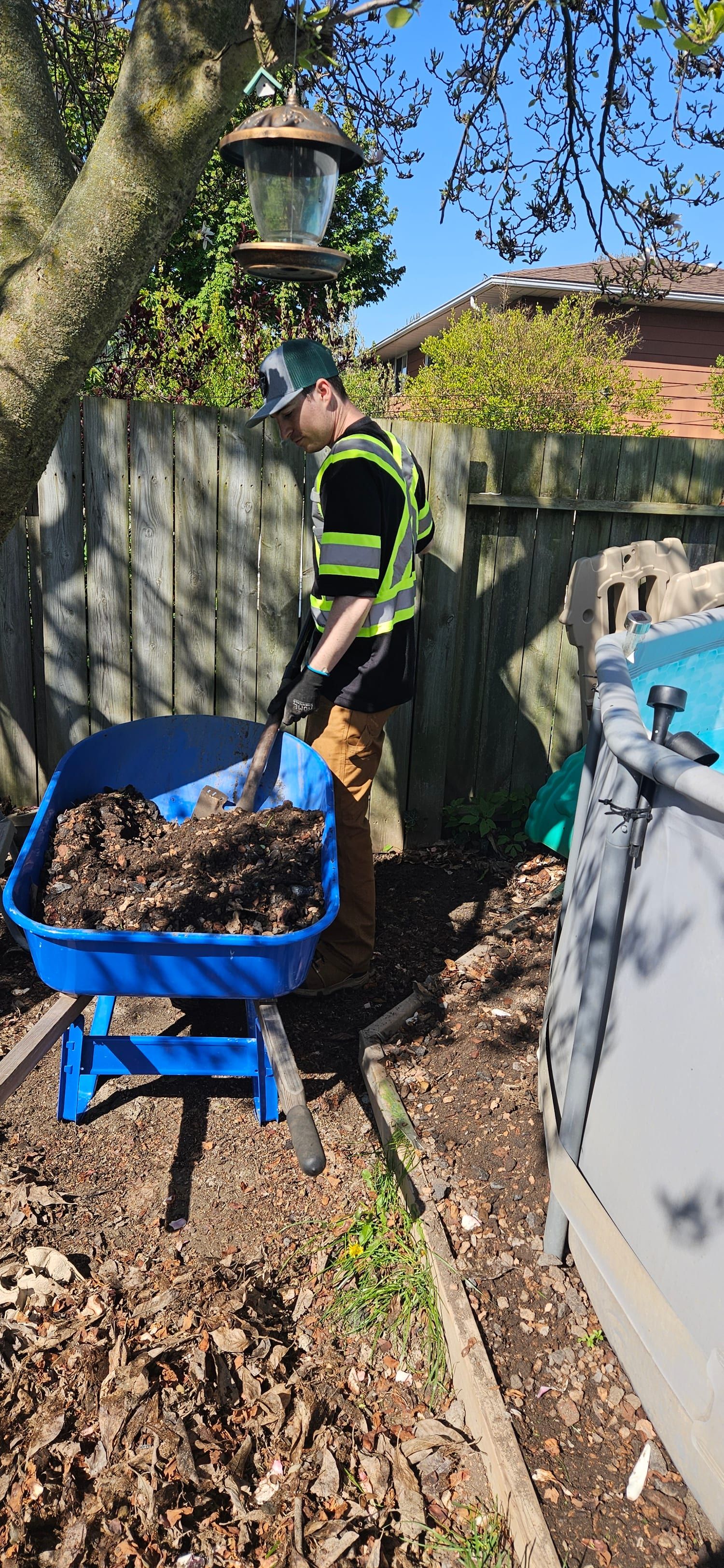 Crew member shovelling compost into a wheelbarrow in a backyard garden