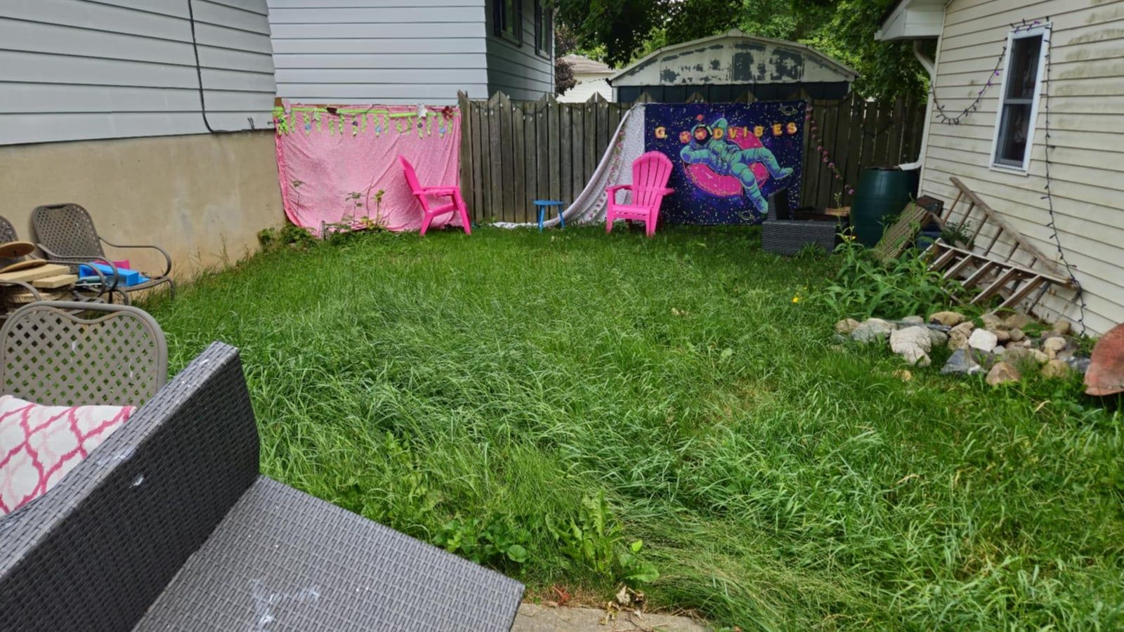 A backyard grown long and shaggy beside the patio furniture before mowing