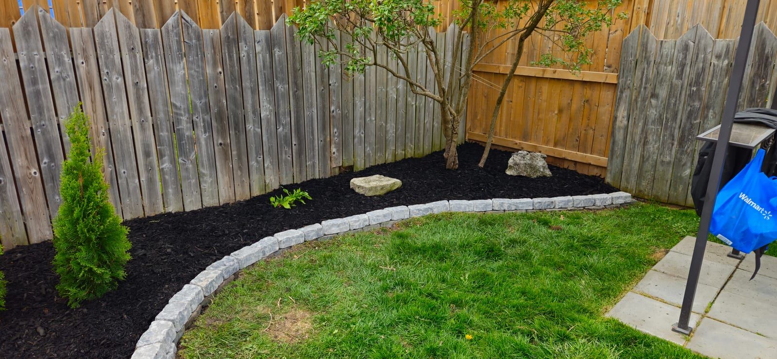 A curved black mulch bed with stone edging along a wood fence