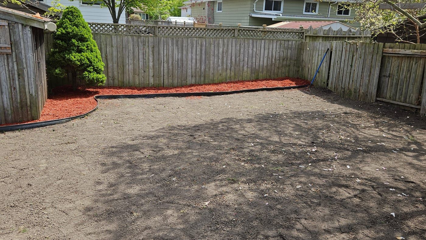 The same backyard partway through, stripped and levelled with the new mulch bed edged along the fence