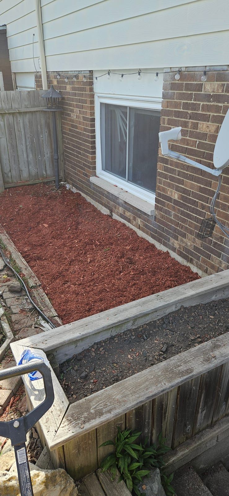 A garden bed along a brick foundation topped with fresh red-brown mulch