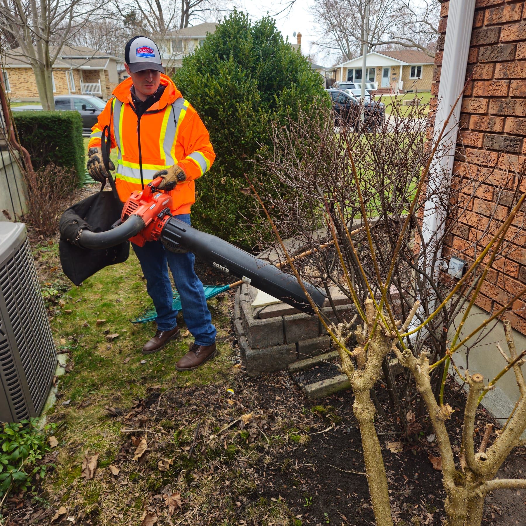 Crew member clearing leaves from a front garden bed with a backpack blower